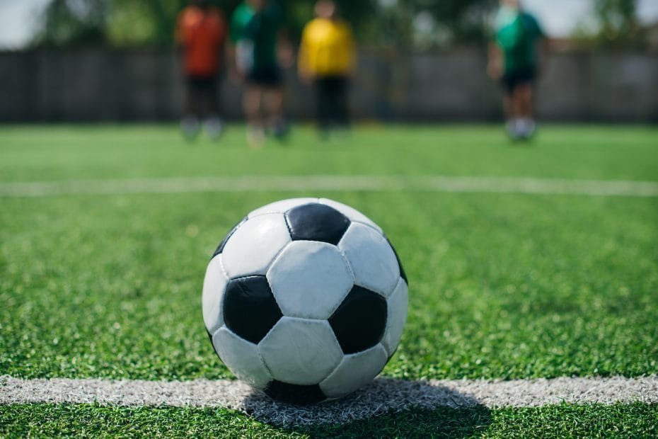 selective focus of football ball and players on green football field